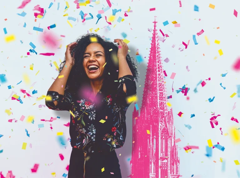 Fröhliche Person im Konfettiregen vor dem Freiburger Münster als Motiv für das Jubi-Gewinnspiel